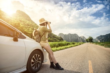 A young woman using black binoculars outside her car on the road of travel