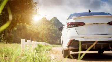 Close-up rear view of a white car with morning light with mountains and sky on the road.