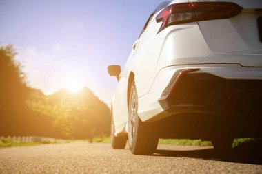 Close-up rear view of a white car with morning light with mountains and sky on the road.