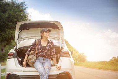 A female traveler rides a hatchback in the light and trees and the morning sky.