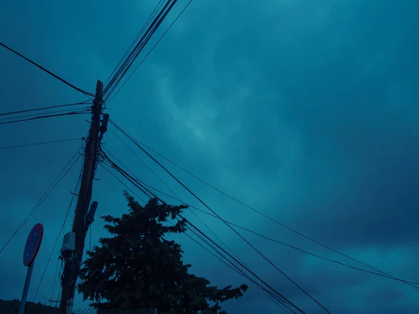 Fırtına bulutları ve biraz güneş ışığı bir direğin ve ağaçların üzerinden yükseliyor..