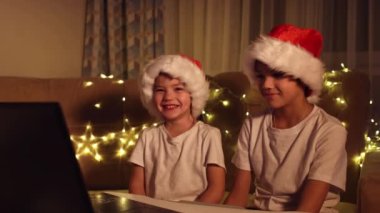 Noel selamları çevrimiçi. Noel Baba 'daki iki küçük çocuk bir dizüstü bilgisayara şapka takıyor. Arkadaşlara, akrabalara ve ailelere video görüşmeleri. Noel konsepti