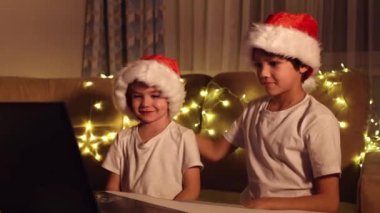 Noel selamları çevrimiçi. Noel Baba 'daki iki küçük çocuk bir dizüstü bilgisayara şapka takıyor. Arkadaşlara, akrabalara ve ailelere video görüşmeleri. Noel konsepti