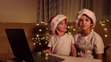 Noel selamları çevrimiçi. Noel Baba 'daki iki küçük çocuk bir dizüstü bilgisayara şapka takıyor. Arkadaşlara, akrabalara ve ailelere video görüşmeleri. Noel konsepti