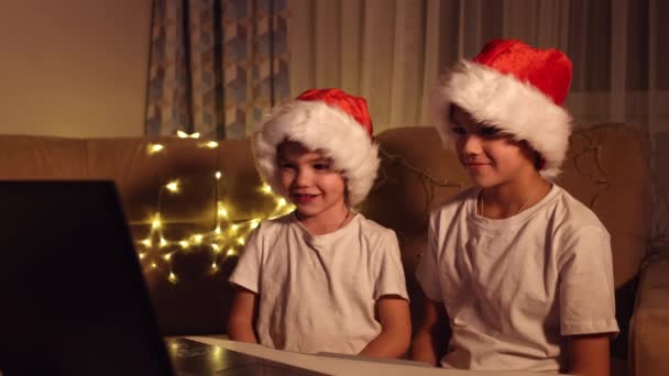 Auguri di Natale online. Due ragazzini a Babbo Natale hanno un portatile. Saluto videochiamate ad amici, parenti e genitori. Il concetto di Natale — Video Stock