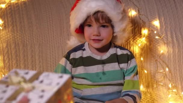 Un garçon ouvrant boîte cadeau à l'arrière-plan des lumières de vacances. Noël. Au ralenti. Émotions positives des gens. — Video