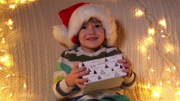 A boy opening present box at holiday lights background. Christmas. Slow Motion. Positive Emotions of People. — Stock Video
