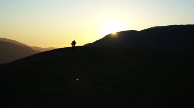 Gün batımında dağlarda bisiklete binen bir bisikletlinin hava görüntüsü.