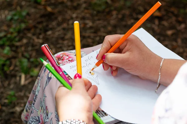 A woman's hand draws a flower with pencils, on her arms, outdoors, relaxation, well-being