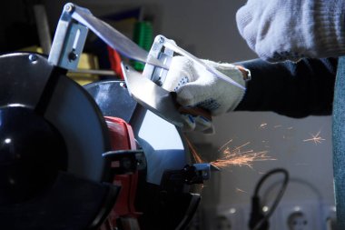 Keskinleştirme makinesi çalışıyor. Bileme makinesinde bıçağı olan bir erkek eli.. 