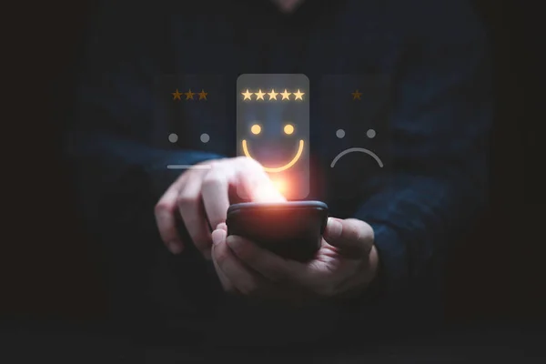 İş adamı, müşteri değerlendirmesi için gülen yüz simgesi ve kullanım ürünü ve servis kavramından sonra müşteri memnuniyeti için akıllı telefon kullanır.