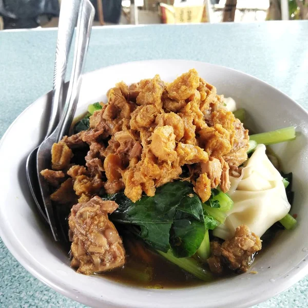 麺と鶏と緑の野菜が美味しいスープが並ぶインドネシアの人気ストリートフード 三重アイアム が道端で食べられています — ストック写真