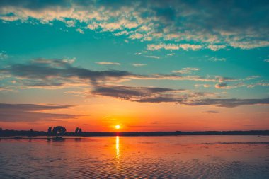 Bright colorful sunset over river. Golden sun reflected in water. Clouds in blue sky. Amazing nature background texture