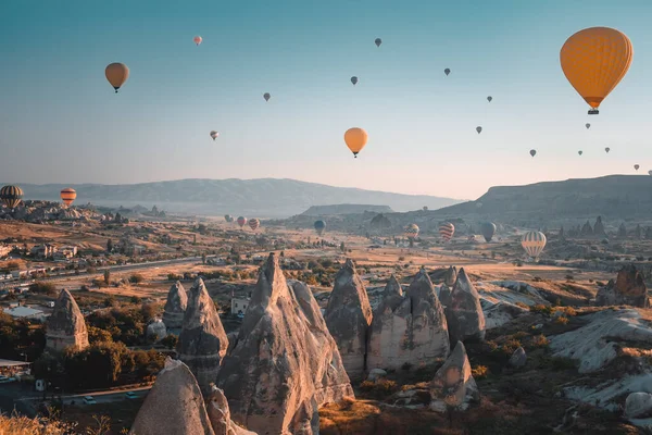 Sunrise in Cappadocia - Turkey travel background. Bright hot air balloons fly over cave houses and famous multi head stone mushrooms in Goreme national park. Tourism, holidays, recreation, destination