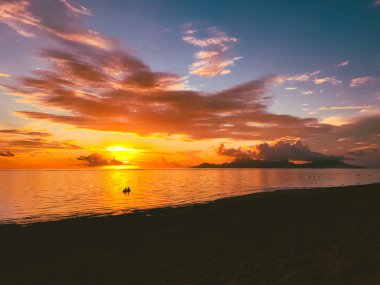 İnsanlar açık turuncu gün batımını, bulutlu gökyüzünü izliyorlar. Güzel doğa manzarası. Etkileyici renkli deniz manzarası. İnanılmaz doğal bir geçmişi var. Popüler turizm beldesi