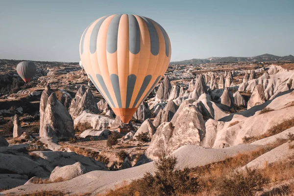 Colorful hot air balloon preparing to rise up for sunset watching tour over spectacular Cappadocia mountains. Wide landscape of Goreme valley. Vintage retro orange blue toning filter. Tourism, travel