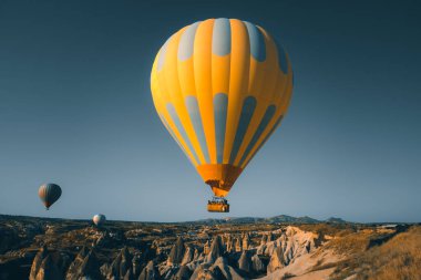Turistlerin güneşin doğuşunu izlemek için kalktıkları sarı, sıcak hava balonu. Kapadokya 'daki Goreme Vadisi' nin geniş mavi gökyüzü manzarası. Turizm, seyahat, tatiller, eğlence geçmişi, konsept kartpostal