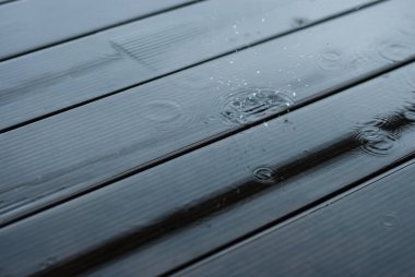 Yağmur damlaları ahşap terasa düşer. Şiddetli yağmur yağıyor. Yerde bir su birikintisi.