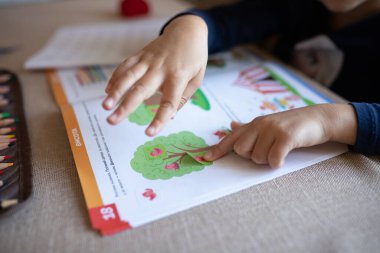 Closeup of a kid hand sticking a sticker on a workbook. Home education, home studying