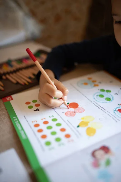A child drawing in a workbook. Home education, home studying