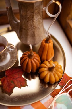 Balkabağı şeklinde mumlar, çay fincanı, penceresinde sonbahar yaprakları, çaydanlık, altın tepsi ve klasik kitapla sonbahar durgun hayatı.