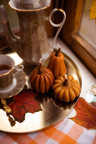 Balkabağı şeklinde mumlar, çay fincanı, penceresinde sonbahar yaprakları, çaydanlık, altın tepsi ve klasik kitapla sonbahar durgun hayatı.