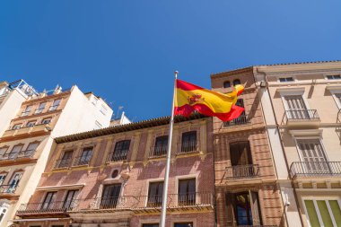 Eski Malaga şehrinde İspanyol bayrağı. Arka planda tipik İspanyol mimarisi olan güzel binalar. Güneşli bir yaz gününde mavi gökyüzü