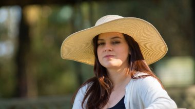 Güzel, uzun saçlı İspanyol bir kadının portresi. Parktaki bankta oturan şapkalı bir kadın. Gün batımında odaksız yeşil ağaçların arka planına karşı düşünceli bir tutum sergiliyor.