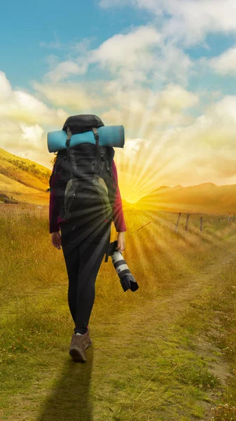 Beautiful Hispanic female explorer seen from behind with backpack walking with a camera in hand in the middle of a sown field on a cloudy morning