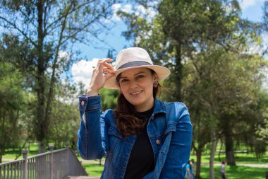 Güneşli bir sabahta parkın ortasında duran şapkalı, gülümseyen güzel İspanyol kadının portresi.