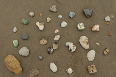 Gün boyunca boş bir plajda farklı renk ve dokulardan oluşan bir grup taşın üst görünümü