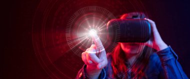 Sanal gerçeklik gözlüklü İspanyol kadın dijital teknolojisiyle siber uzayı mavi ve kırmızı ışıkla keşfederken parmağıyla ışık düğmesine basıyor.