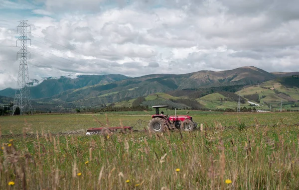 Red Tractor Plowing Field Green Grass Mountains Background Day Cloudy — ストック写真