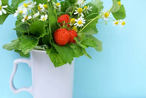 Tea set with chamomile flowers, strawberries and mint in a purple mug
