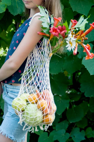 Set of vegetables, fruits and flowers stacked in a wicker net outdoors in summer
