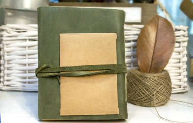 Olive leather notebook with a piece of craft paper and a skein of thread on a light background