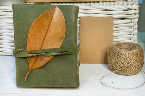 Olive leather notebook with a piece of craft paper and a skein of thread on a light background