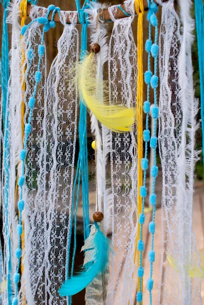 Dream catchers crocheted from threads on a wooden base in the colors of the Ukrainian flag, namely in yellow and blue, decorated with lace, threads, feathers and wooden beads on the street