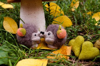 A date under a mushroom made of pumpkin and salt dough by two felted hedgehogs during the day surrounded by green grass, felted hearts and yellow leaves