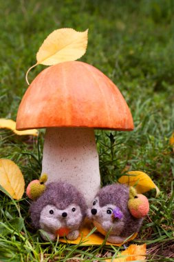 Date under a mushroom made of pumpkin and salt dough, two felted hedgehogs during the day surrounded by green grass and yellow leaves