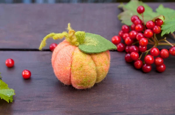 Pumpkin made using the technique of dry felting on wooden boards surrounded by viburnum berries