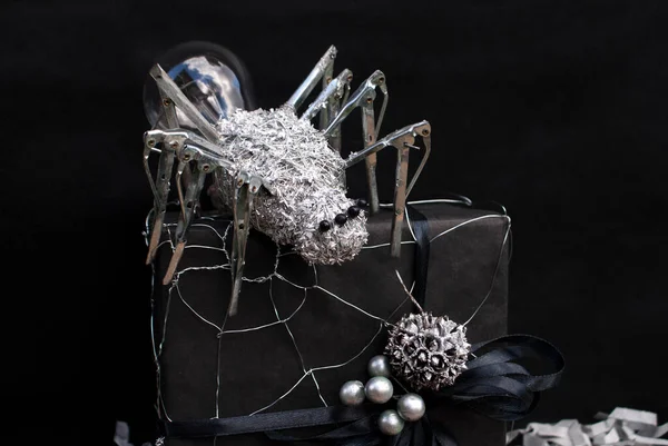 This metal spider is made with a light bulb, umbrella needles, metal wire, beads and metal shavings with a wire web on a black gift