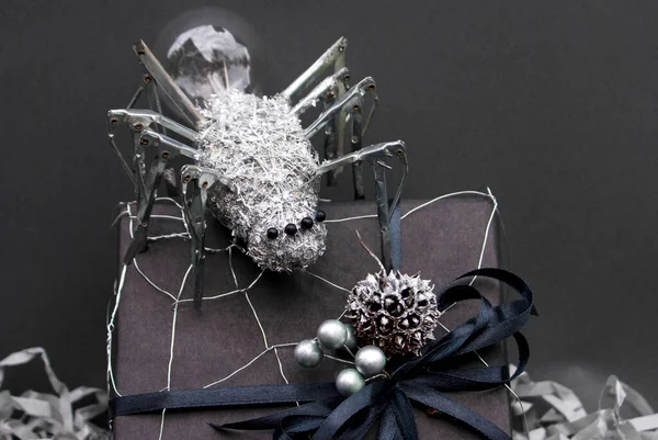 This metal spider is made with a light bulb, umbrella needles, metal wire, beads and metal shavings with a wire web on a black gift