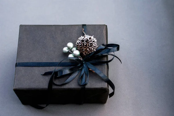 Black gift with a black ribbon, silver berries and a thorn on a gray background