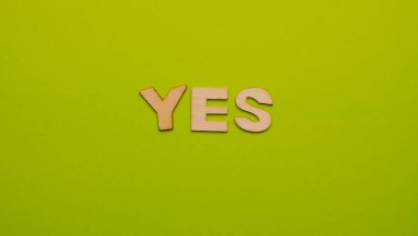 Wooden letters on plain colored background with the word written in English: Yes