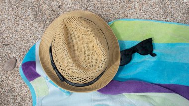 Yellow straw hat shade towel of blue and green colors on the white sand and next to sunglasses