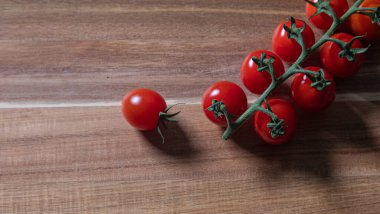 Small deep red cherry tomatoes on a branch on a weathered wooden board