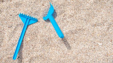 Blue toy plastic shovel and rake on the white sand of the beach