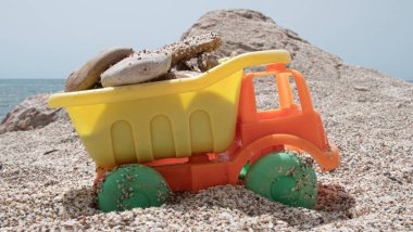 Orange and yellow plastic toy truck loaded with stones on the beach