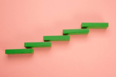 Ladder or graph built with green colored wooden pieces on light pink background
